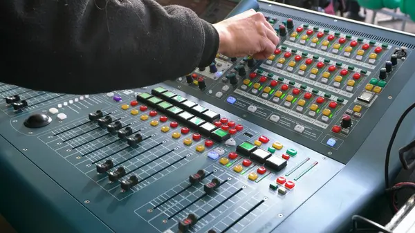 Hands move the levers of the mixing console to record and amplify the sound.