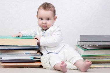 Kitapların arasında küçük bir çocuk. Bir yığın kitabın içinde mutlu bir altı aylık erkek bebek. Erken eğitim kavramı.