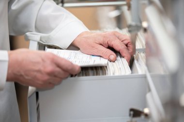 The nurse's hands are looking in the archive for a patient's card. The file is in a cell in the clinic. clipart