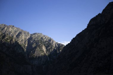 Mavi gökyüzüne karşı karanlık, kasvetli dağlar.