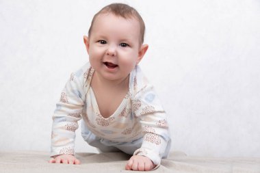 Beyaz arka planda gülümseyen bir çocuk. Altı aylık sevimli bir bebek yatakta emekliyor. Babalığın ve anneliğin kavramsal fotoğrafı.