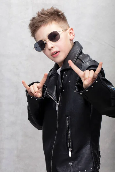 一个戴太阳镜的重金属男孩的画像 穿着皮夹克做摇滚标志的可爱少年 — 图库照片