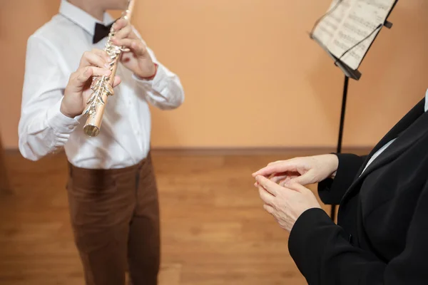 A music teacher listens to a student playing the flute in a music school.