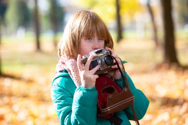 Sonbahar parkında elinde retro kamera olan kızıl saçlı küçük bir kız. Çocuk fotoğrafçısı.
