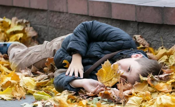 Ένα Χαρούμενο Παιδί Κείτεται Στα Φθινοπωρινά Φύλλα Της Πόλης Ζεστό — Φωτογραφία Αρχείου