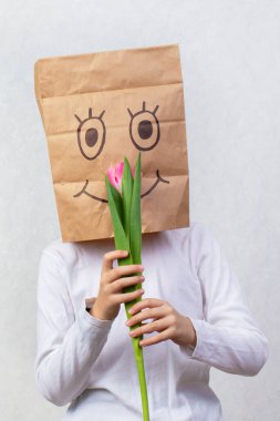 Çocuğun kafasına boyalı gülümsemeli bir karton hediye çantası konuldu. İsimsiz hediye konsepti.