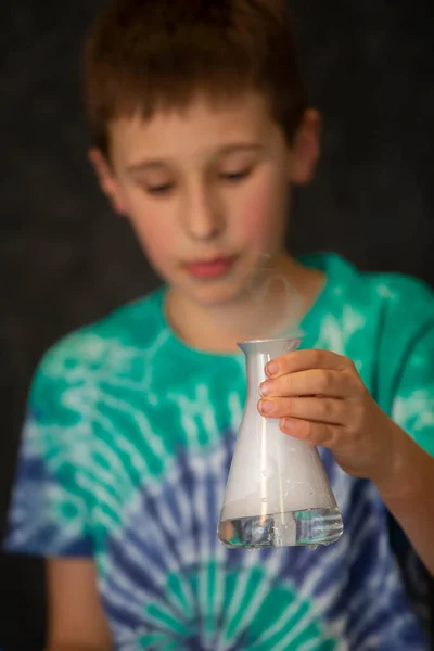 A boy conducts a scientific chemical experiment with liquid nitrogen. A child with a glass flask filled with smoke.