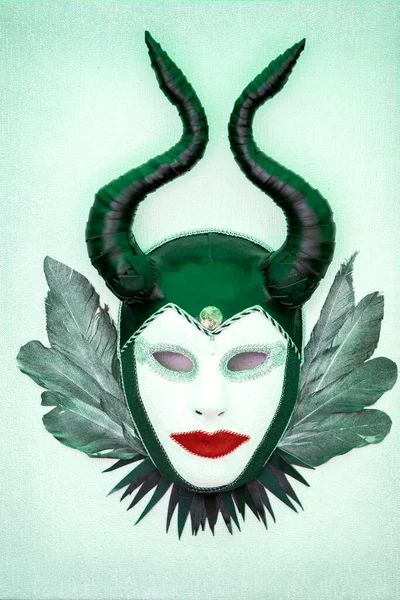 Abstract theatrical mask with horns and feathers on a green background.