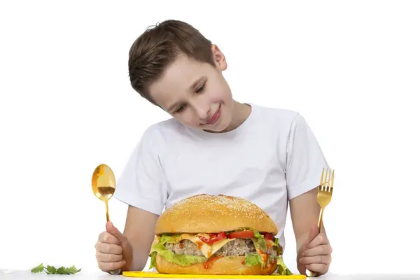 小男孩与大汉堡包隔离在白色 一个少年拿着一把金叉和一把勺子 — 图库照片