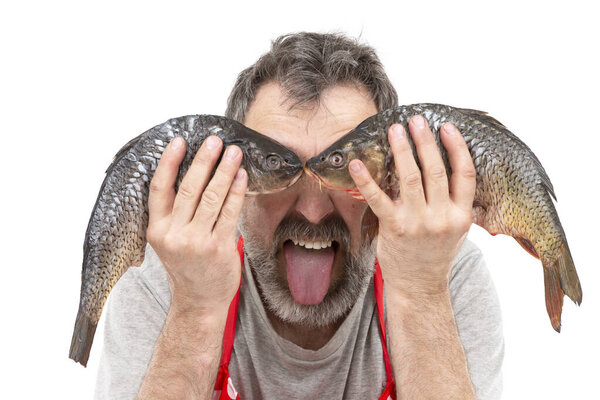 Funny bearded merchant or cook holding raw freshwater fish at eye level and showing tongue. Cheerful seller from the fish market. The chef is joking.