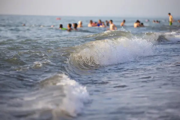 Sea wave on the background of blurred people swimming in the sea.