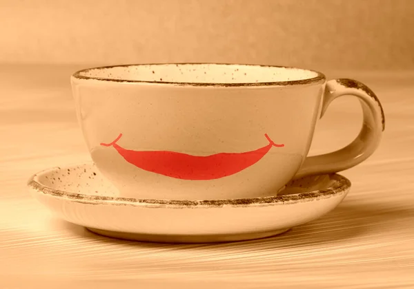 Ceramic cup with a painted smile in beige toning. Morning coffee or tea with a good mood.