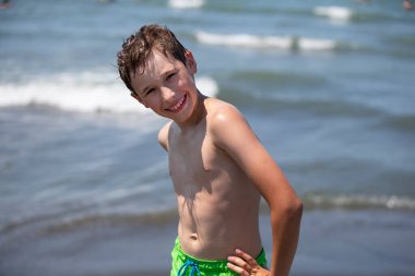 Mutlu çocuk deniz kenarında dinleniyor, kameraya bakıyor. Çocuk deniz kenarında tatilde..