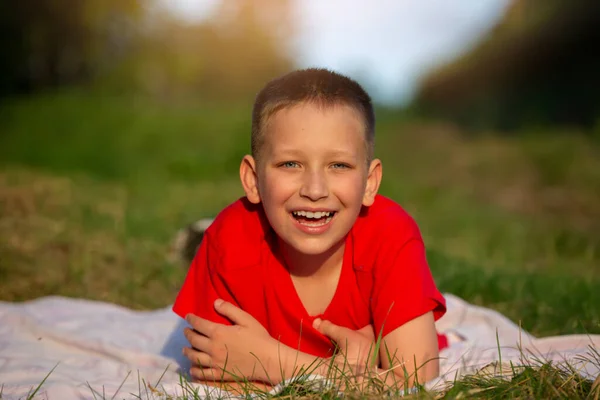 幸せな少年は笑顔で草の上に横たわり カメラを見ている — ストック写真