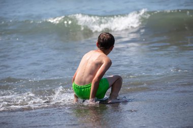 Mutlu çocuk denizde yüzüyor, dalgalarla oynuyor. Çocuk deniz kenarında tatilde..