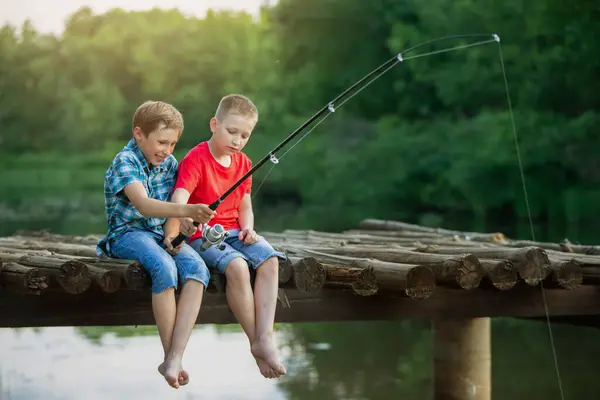 两个男朋友坐在一座木桥上钓鱼 钓鱼之旅的孩子 — 图库照片