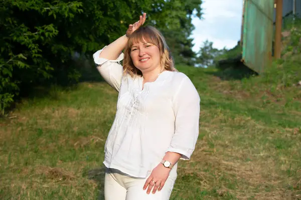 A middle-aged woman of large build against the background of summer greenery.