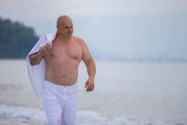 Yaşlı, yakışıklı, atletik yapılı bir adam sahil boyunca yürüyor..