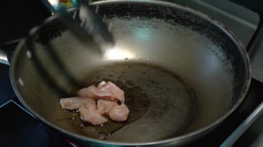 Şef tavuklu filetoyu her zamanki sebze yağı malzemeleriyle birlikte tavada kızartıyor. Aşçı tavuk parçalarını ileri geri pişirir..