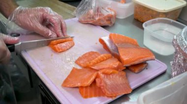 Aşçının elinin yakın çekimi Şef somon filetosu keser. Profesyonel bir adam kırmızı balık keser. Geleneksel Japon yemeği dilimlenmiş sashimi. Suşi hazırlığı.