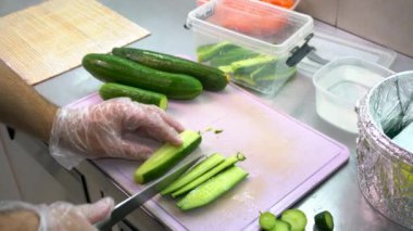 Geleneksel Asya mutfağı için bıçakla sebze doğrayan bir şefin ellerine yakın çekim. Profesyonel bir suşi şefi salatalık keser..