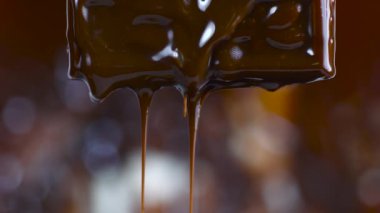 Erimiş çikolata damlıyor. Erimiş çikolatayı koyu bir arka plana damlatarak..
