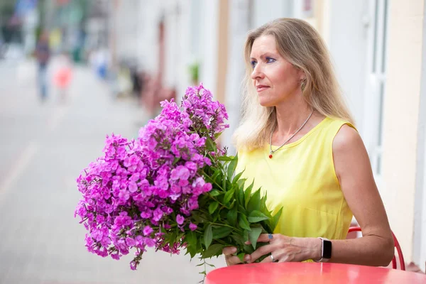 Beautiful elderly blonde woman with a huge bouquet of flowers.