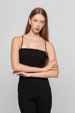 Gri arka planda siyah tişörtlü, mavi gözlü güzel sarışın kız. Manken ellerini kavuşturdu..