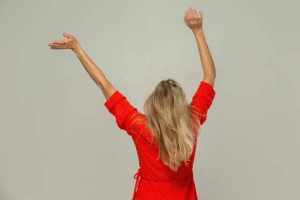 Blonde woman turned her back to the camera and waves her arms.Isolated on a gray background.