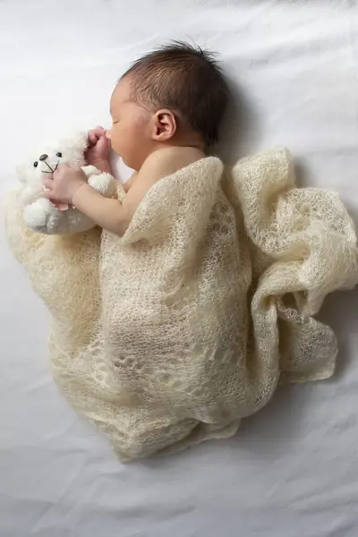 Newborn baby wrapped in a knitted blanket on a light background.