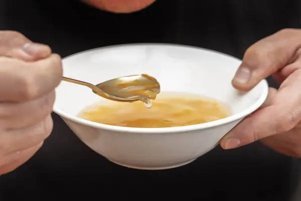 Hands holding a plate of chicken soup and a spoon.