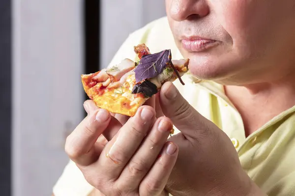 The man\'s hands hold a piece of pizza to his mouth.