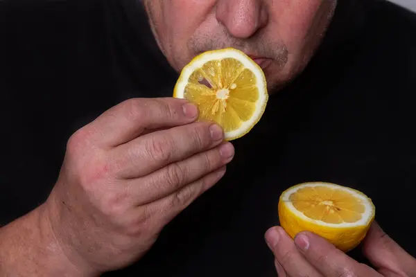 An unrecognizable man eats a sour lemon.