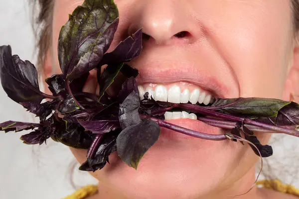 The woman, whose face is not visible, holds a basil branch in her mouth. Eat greens
