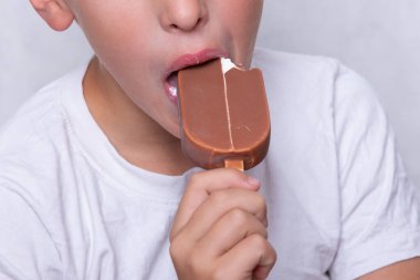 Yüzü tanınmaz halde olan bir çocuk çikolata kaplı dondurma yiyor..