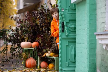 Turuncu elbiseli bir çocuk Cadılar Bayramı 'nda balkabağıyla süslenmiş bir evin kapısından dışarı bakar..