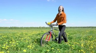 Bisikletli güzel sarışın bir kız karahindiba tarlasında yürüyor..