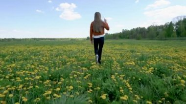Uzun saçlı genç bir sarışın karahindiba bahar tarlasında yürüyor. Doğayı seviyor..