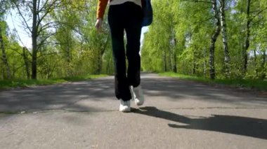 Sırt çantalı bir kızın bacakları asfalt yolda yürüyor..