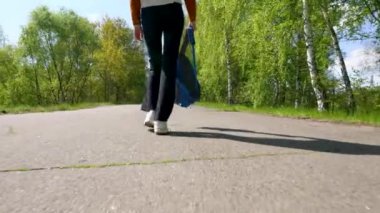Sırt çantalı bir kızın bacakları asfalt yolda yürüyor..