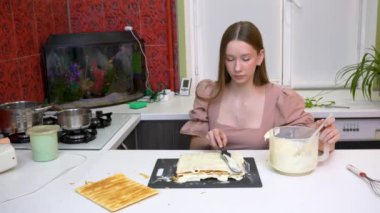 Mutfakta bir kız pasta yapıyor. Puf böreği tabaklarına krema sürüyor..