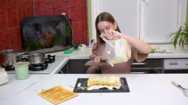 Mutfakta bir kız pasta yapıyor. Puf böreği tabaklarına krema sürüyor..