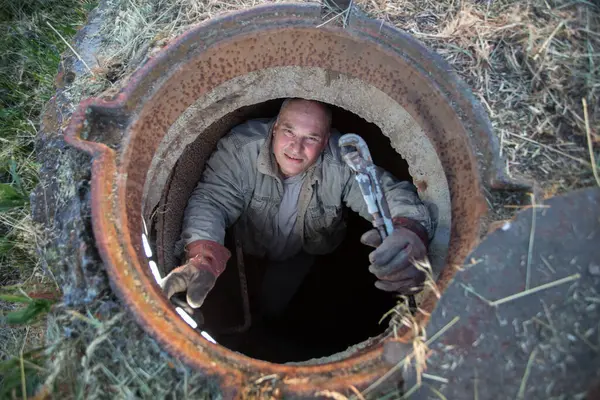 stock image Sewage works. Industrial wastewater treatment. A worker in a sewer hatch with a plumbing key.