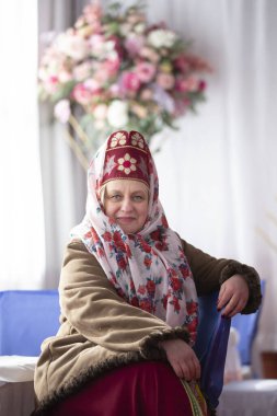 Ulusal başlıklı, güzel, yaşlı bir Rus kadın Kokoshnik ve koyun derisi ceketli. Gülümsüyor ve kameraya bakıyor..