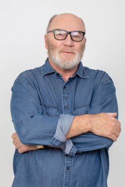 Gri arka planda izole edilmiş kot gömlek giyen, gözlüklü, beyaz saçlı çekici bir adamın portresi..