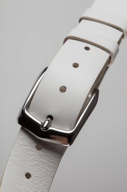 Gri bir arka planda tokası olan beyaz deri klasik kemerin bir parçası..