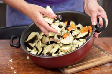 Eller patlıcanları pişirmek için tavaya koyar. Sebzelerden sağlıklı yemekler hazırla.