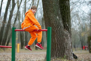 Genç bir çocuk yatay çubuklarla meşgul, parkta egzersiz yapıyor..