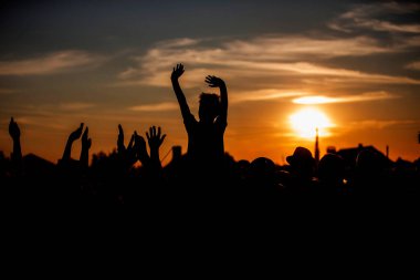 Tanınmayan bir grup insan, bir konser veya halka açık bir etkinlikte güneşin batışına karşı el sallıyor. Gece müzik festivali.