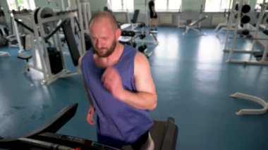 Atletik yapılı bir adam spor salonundaki koşu bandında koşar..